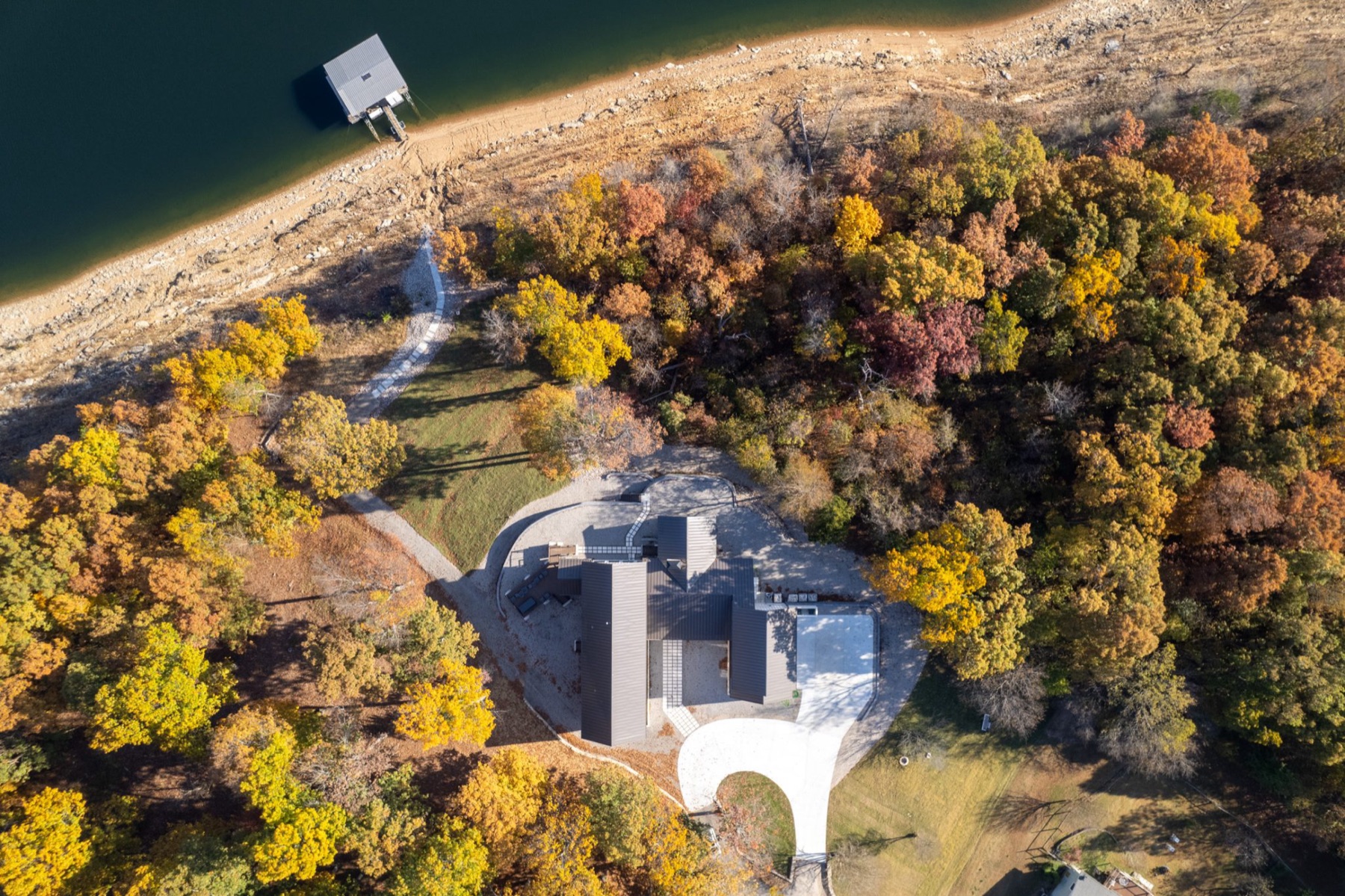 Aerial view of a lakefront custom home surrounded by autumn woods