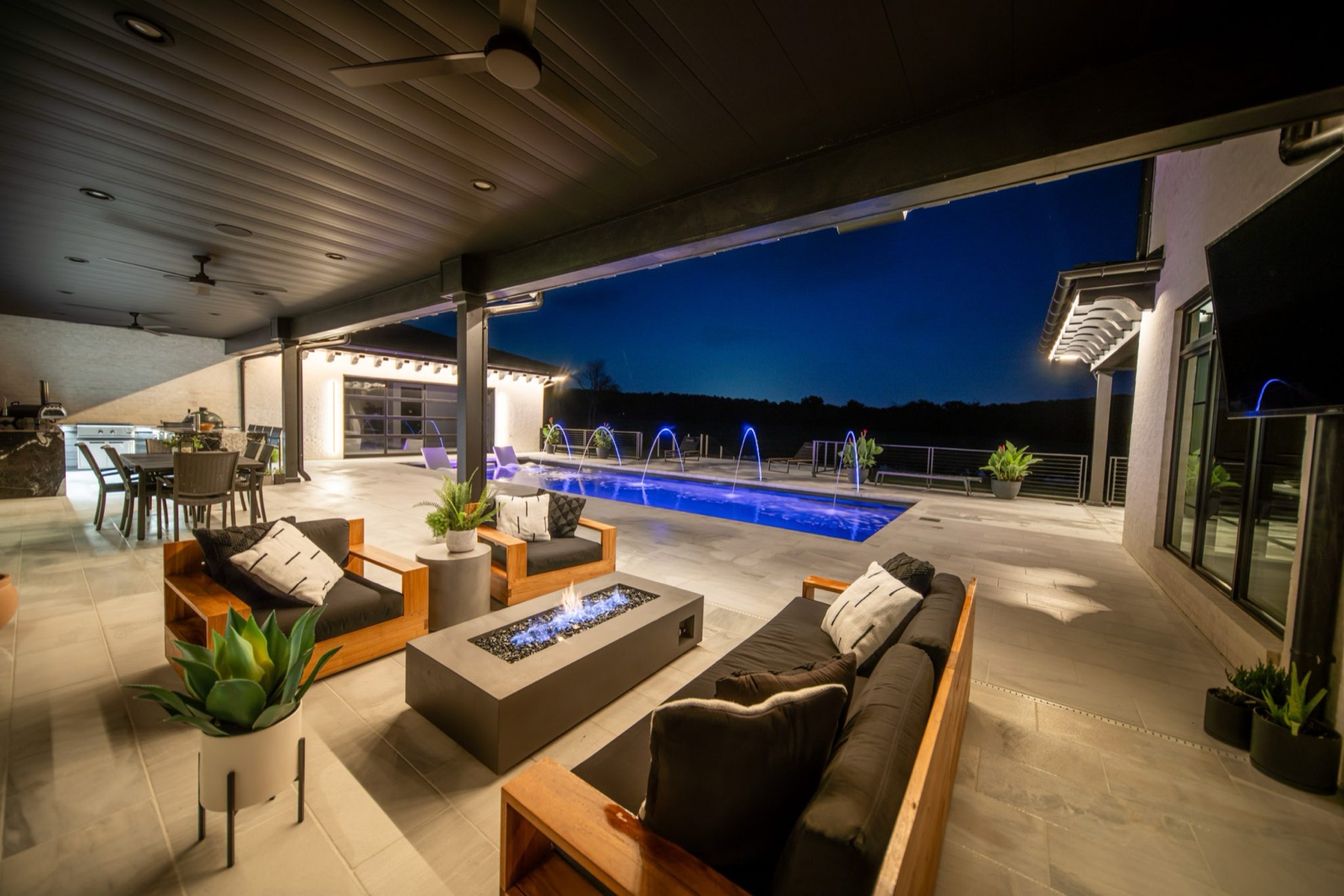 Covered outdoor living area with pool and fire table at night